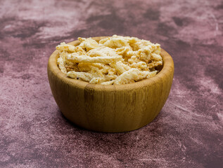 Breaded fried onions in a small wood bowl atop a maroon background.