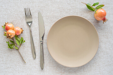 Table setting with empty plate, cutlery, wild pomegranate fruits on cotton fabric background.