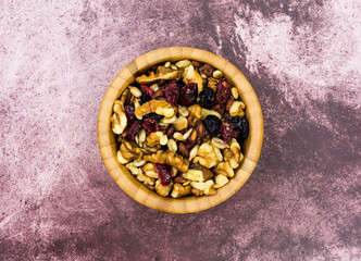 Overhead view of a wood bowl filled with healthy trail mix on a tabletop.