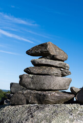 Stack of rocks upon a large boulder with a bright blue sky and clouds in the background.