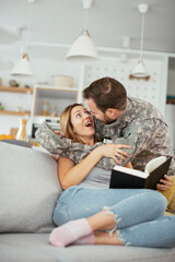 Happy soldier and his wife sitting on sofa at home. Young soldier hugging wife..