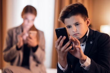 A kid texting messages on his smartphone, his older sister in the back is also on her cell phone.