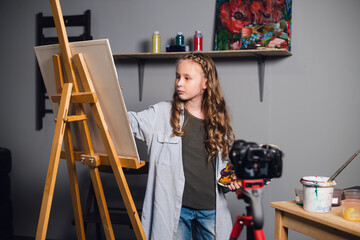 a cute teen artist is recording a story for her video blog in a workshop at an art school