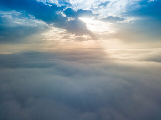 Aerial drone flight over the fog. There are thick clouds of fog below, the sun breaks through the clouds.