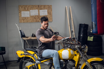 Fototapeta na wymiar A brutal biker buys a yellow powerful motorcycle. He checks it in the garage