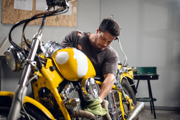 Fototapeta na wymiar A young sports motorcycle repairman in a garage or workshop is working on a yellow bike