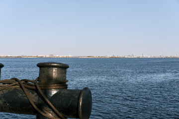 Naklejka premium Maritime hemp rope and chain moorings on a black cast iron bollard on the ship. Cityscape on the other side of river. used principally for mooring boats