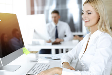 Obraz premium Blond business woman using computer at workplace in sunny office. Working for pleasure and success