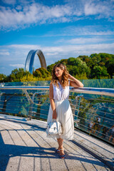 a girl in a white dress is walking under the rainbow building on a summer day. 