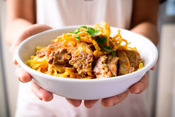 Northern Thai food (Khao Soi), Spicy curry noodles soup with beef in a bowl holding by hand