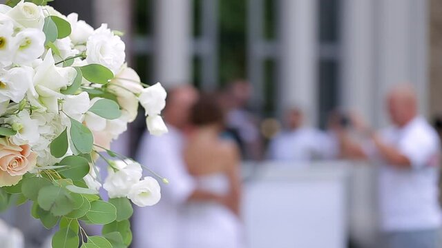 A bouquet of white flowers in the left corner of the video against a blurred background, where people are being photographed. Free space for the text.