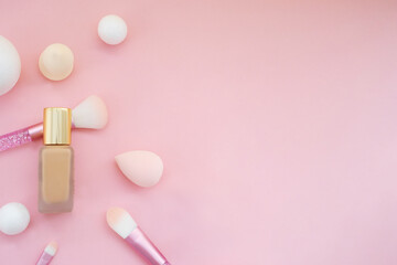 
bottle with make-up foundation, brushes and sponges for application on a pink background. Copy space