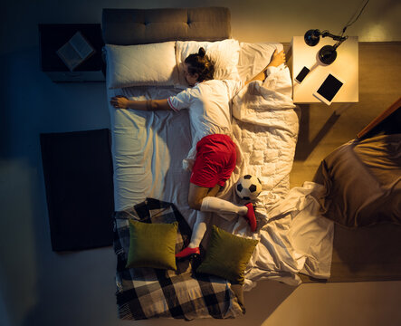 In love. Top view of young professional football, soccer player sleeping at his bedroom in sportwear with ball. Loving his sport, workaholic, playing match even if resting. Action, motion, humor.