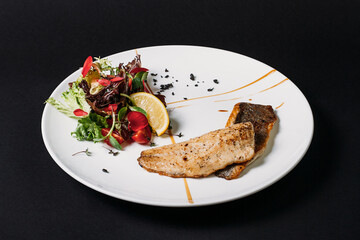 Fried fish in white plate on a black background with lime. 
