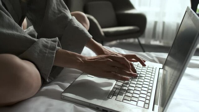 close-up of a woman in a bathrobe working at a laptop in bed removed