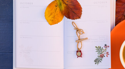 Daylight Saving Time & Fall Concept. Red Alarm Clock and Autumn Bright Leaves on Open Page of Notebook - Background, Copy Space. Enjoy Extra Hour and Cup of Coffee - Little Pleasures.