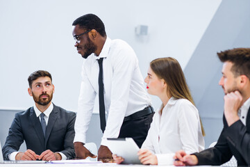 Serious diverse colleagues brainstorm at conference table discuss project at meeting, focused business people talk negotiation in office at briefing, business partners speak considering cooperation