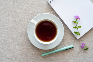 Top view of tea cup, blank notebook paper, pen on cotton fabric background. Tea break concept.