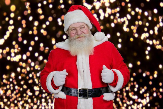 Portrait of bearded smiling Santa Claus. Authentic Santa Claus in costume and hat standing on New Year lights background. Old kind Santa Claus.