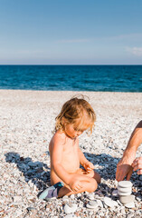 Toddler girl and man playing with pebbles on beach