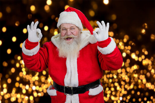 Santa Claus making ok sign with both hands. Happy Santa Claus with real beard showing okay gesture standing on New Year lights background. Portrait of cheerful Santa. New Year concept.