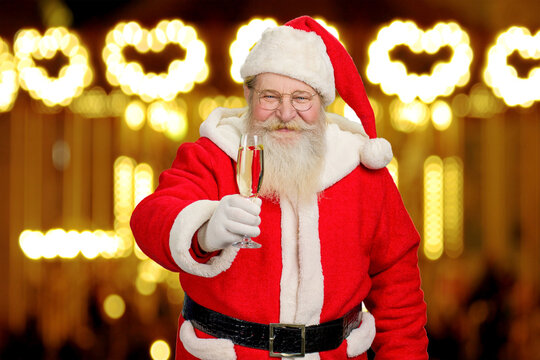 Santa Claus holding glass of champagne. Happy Santa Claus with a glass of sparkling champagne on New Year lights background. New Year greeting from Santa Claus.