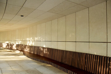 A wooden bench with a back is installed along the marble wall. Light falls on a bench in a stone passage.