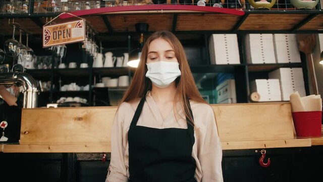 Portrait of owner restaurant wearing protective mask looking at camera. Young coffee shop owner or waitress in medical mask waites clients. Small business reopen after lockdown.