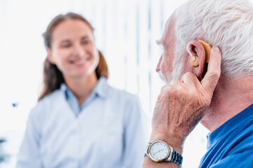 Focused picture of an elderly male patient with hearing aid side view with blurred woman doctor in...