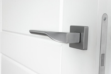 The silver metal doorknob is mounted in a white wooden door