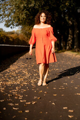 A beautiful woman with curly dark hair in a red dress walks through the autumn city. Autumn mood,...