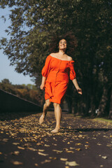 A beautiful woman with curly dark hair in a red dress walks through the autumn city. Autumn mood,...