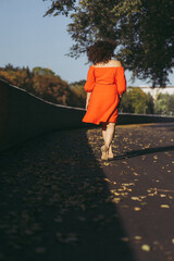A beautiful woman with curly dark hair in a red dress walks through the autumn city. Autumn mood,...