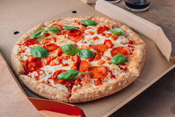 Pizza box delivery concept. Open box with hot tasty italian sliced pepperoni pizza with basil. Selective focus