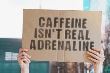 The phrase " Caffeine isn’t real adrenaline " on a banner in men's hand with blurred background. Coffee. Tea. Substance. Drink. Addicted. Addiction