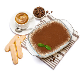 Traditional Italian Tiramisu dessert in glass baking dish, savoiardi cookies and cup of fresh espresso coffee isolated on white background with clipping path