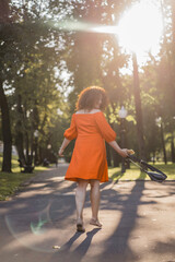 A beautiful woman with curly dark hair in a red dress walks through the autumn city. Autumn mood,...