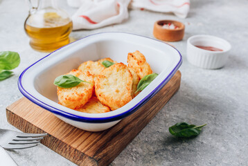 Hash brown or potato pancakes on enameled bowl wooden board with catsup on light gray background.