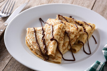 Sweet crepes with chocolate on wooden table
