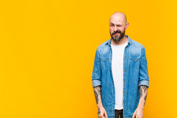 young bald and bearded man looking happy and friendly, smiling and winking an eye at you with a...