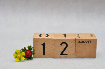 12 August on wooden blocks with a strawberry and yellow flower on a white background