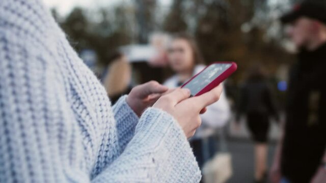 Woman using smartphone outdoor walking with gadget on city street people and cars background. Close up hands typing message.