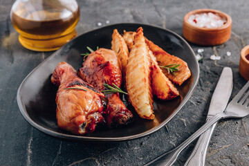 Chicken drumsticks with french fries on black plate on rustic black background.