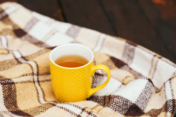Beige plaid and a yellow cup of tea. The concept of home comfort and autumn mood. Copy space