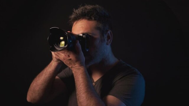 Professional male photographer taking and reviewing a photo and nodding. Positive outcome after a picture taking with a mirrorless camera. Dark photography studio with black background.