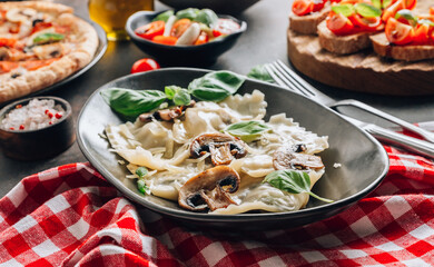 Italian cuisine - ravioli pasta with champignon mushrooms and parmesan cheese on black plate on dark background.