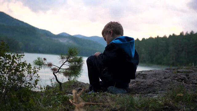 A child is sitting on the riverbank on a cliff. Evening time