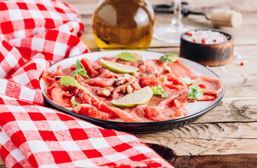White plate with carpaccio of beef with baby arugula, lime and white wine on rustic wooden background.
