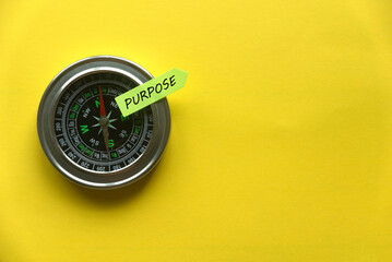 Top view of a compass and sticky note written with Purpose on yellow background with copy space.