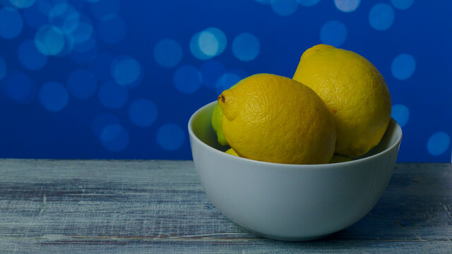 Limones  en un cuenco blanco sobre una mesa blanca y fondo azul